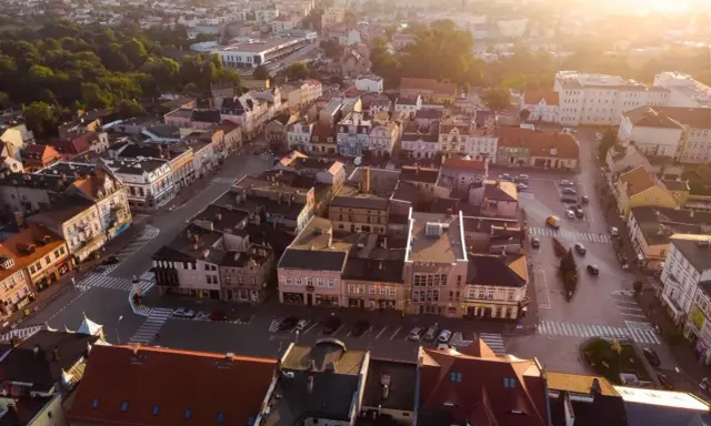 Widok z lotu ptaka na szamotuły rynek z kolorowymi kamienicami i ulicami oświetlonymi zachodzącym słońcem.