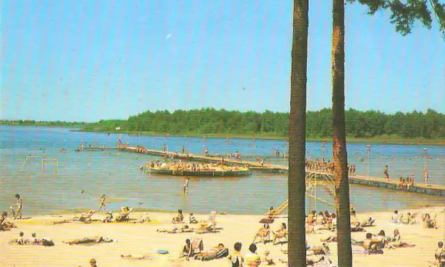 Słoneczny dzień nad jeziorem Niedzięgiel. Ludzie odpoczywają na plaży i pływają, a na wodzie unosi się platforma rekreacyjna.