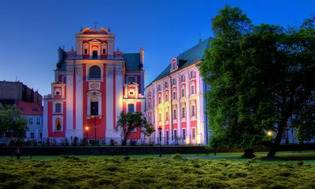 Piękna poznańska trasa spacerowa z zabytkowymi budynkami oświetlonymi wieczorem i bujną zielenią.