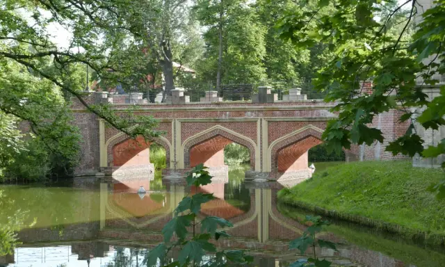 Mostek przy zamku w Kórniku, z cegły, z łukami odbijającymi się w wodzie.