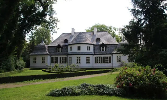 Malowniczy dwór w Koszutach otoczony zielenią. Klasyczna architektura z wieżyczkami i mansardowym dachem.