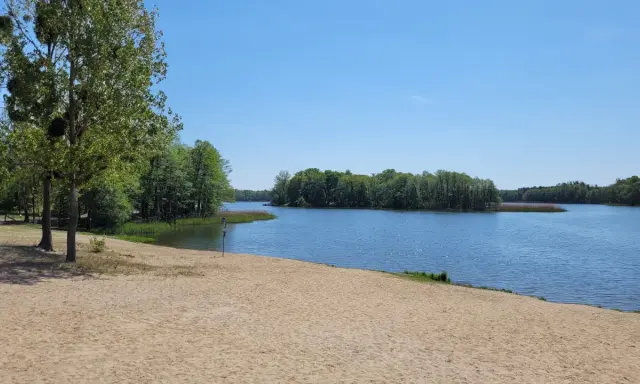Piękny dzień nad jeziorem w Wielkopolsce. Piaszczysta plaża, spokojna woda i zielone drzewa tworzą idealne miejsce na wypoczynek.