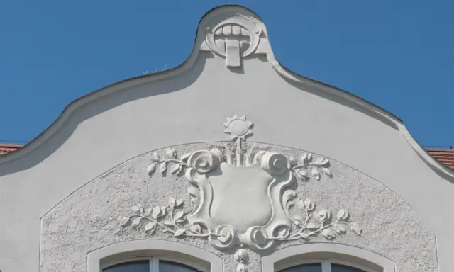 Ozdobny detal architektoniczny w stylu secesja w Poznaniu: tarcza z motywami roślinnymi i groteskowa twarz na szczycie.