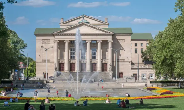 Teatr Wielki w Poznaniu z fontanną i ludźmi odpoczywającymi na trawie to jedne z fajnych miejsc w Poznaniu na spotkanie.