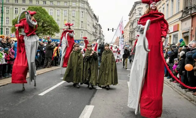 Parada z okazji św. Marcina. Postacie na szczudłach w czerwonych strojach i dzieci w zielonych płaszczach idą ulicą. Legenda o św. Marcinie ożywa.