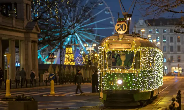 Świąteczny tramwaj po poznańsku, ozdobiony tysiącami lampek, mknie przez miasto. W tle widać diabelski młyn i iluminacje.