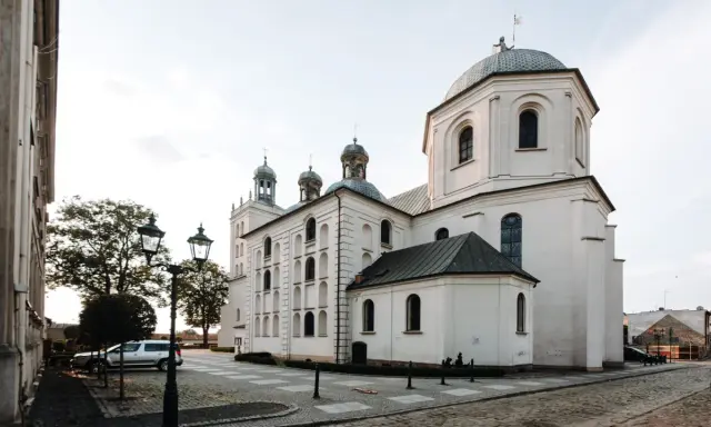 Majestatyczna fara w Grodzisku Wlkp. z charakterystycznymi kopułami i wieżami, otoczona brukowanym placem i zabytkowymi latarniami.