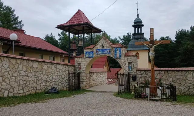 Kamienny łuk z mozaikami i dzwonnicą prowadzi do klasztoru, jednego z wielu pustelni w Polsce. Obok krzyż z Jezusem.