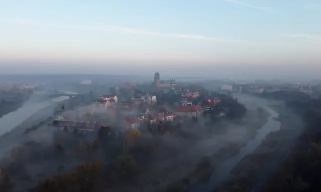 Mglisty poranek nad rzeką, wyłaniający się z mgły **Ostrów Tumski Poznań** z katedrą i zabytkową zabudową.