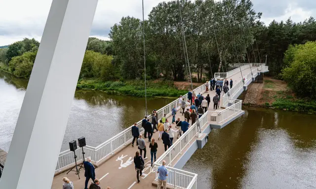 Uroczyste otwarcie kładki owińskiej. Ludzie spacerują po nowoczesnym moście wiszącym nad rzeką, otoczonym zielenią.