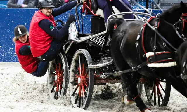 Para jeźdźców w czerwonych kamizelkach w akcji podczas Cavaliady. Dynamiczna jazda zaprzęgiem po piaszczystym torze.