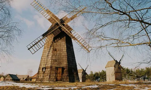 Drewniane wiatraki, jeden duży i dwa mniejsze, stoją na tle nieba i nagich drzew. W oddali widać zabudowania. To malowniczy **osiek nad Notecią**.