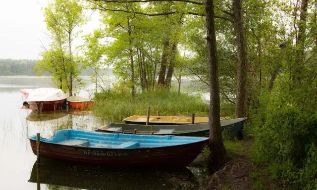 Łodzie zacumowane nad jeziorem w Sierakowskim Parku Krajobrazowym. Wiosna w pełni, drzewa zielone, woda spokojna.