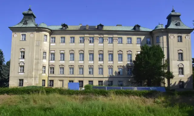 Imponujący pałac, największy zamek w Wielkopolsce, z zielonymi dachami i licznymi oknami, otoczony drzewami i trawą.