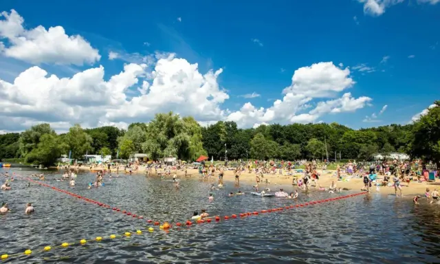 Tłum ludzi odpoczywa na plaży i kąpie się w jeziorze w Poznaniu. Słoneczny dzień, błękitne niebo z chmurami.