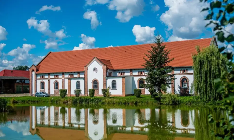 Pałac w Racocie z czerwonym dachem i białymi ścianami odbija się w spokojnej tafli wody.