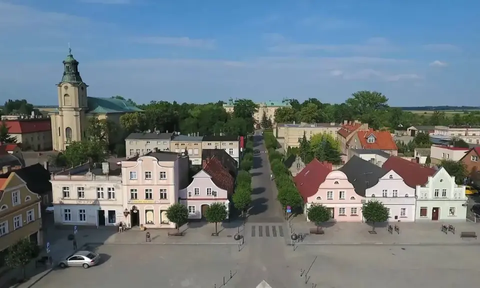 Rydzyna atrakcje: malowniczy rynek z kolorowymi kamieniczkami, kościołem i pałacem w tle.