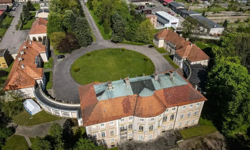 Pałac w Pawłowicach z lotu ptaka, otoczony zielenią i innymi budynkami.