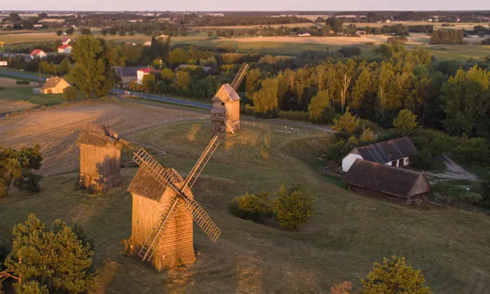 Trzy drewniane wiatraki na tle krajobrazu, przypominające o dawnych pojezierza w polsce.