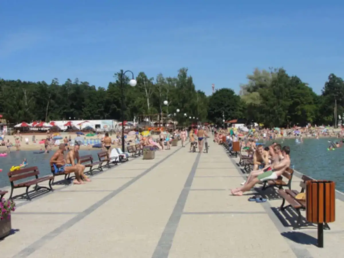 Ludzie odpoczywają na pomoście nad jeziorem Niedzięgiel, w tle plaża i las.