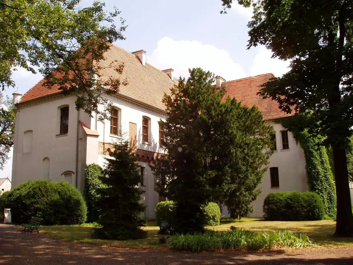 Zamek w Szamotułach otoczony zielenią, z białymi ścianami i czerwoną dachówką.