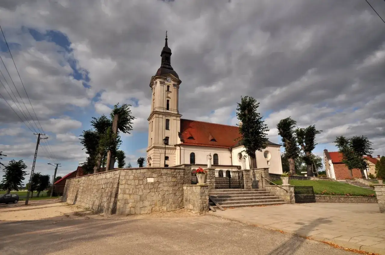 Kości&oacute;ł z wieżą i czerwoną dachem, otoczony kamiennym murem. Miejsce to jest prawdziwą g&oacute;rką duchowną, gdzie spok&oacute;j i piękno natury sprzyjają refleksji.