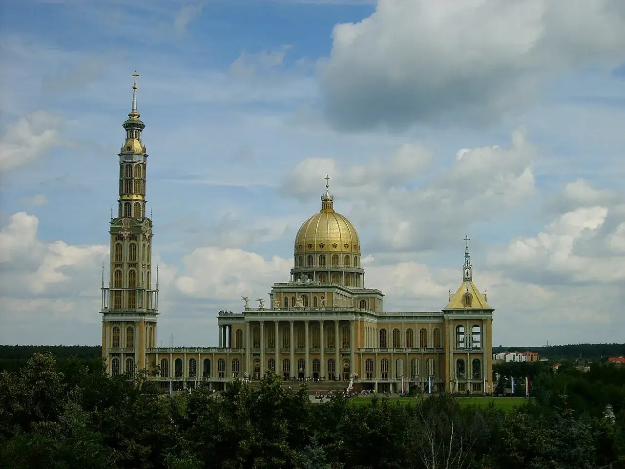 Bazylika w Licheniu, symbol polskiej historii i wiary, z dominującą wieżą i złotą kopułą, na tle błękitnego nieba z chmurami.