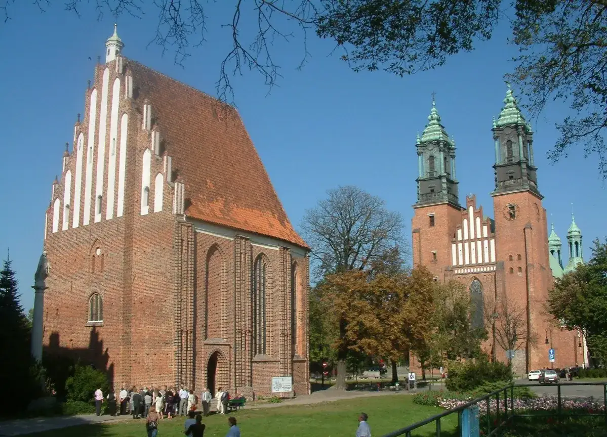 Katedra poznańska, najstarszy kości&oacute;ł w Polsce, z charakterystycznymi wieżami i ceglaną fasadą, otoczona zielenią.