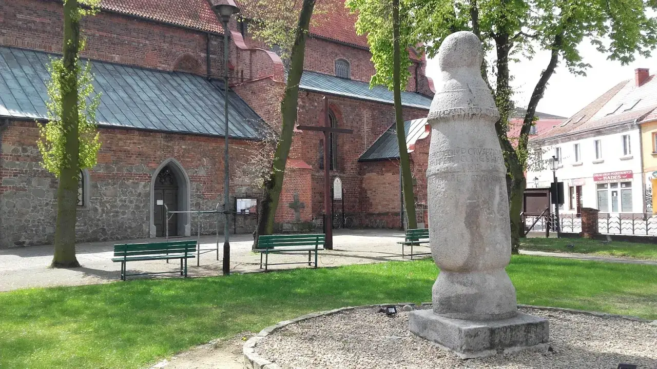 Kamienny słup milowy z inskrypcją stoi przed ceglanym kościołem.