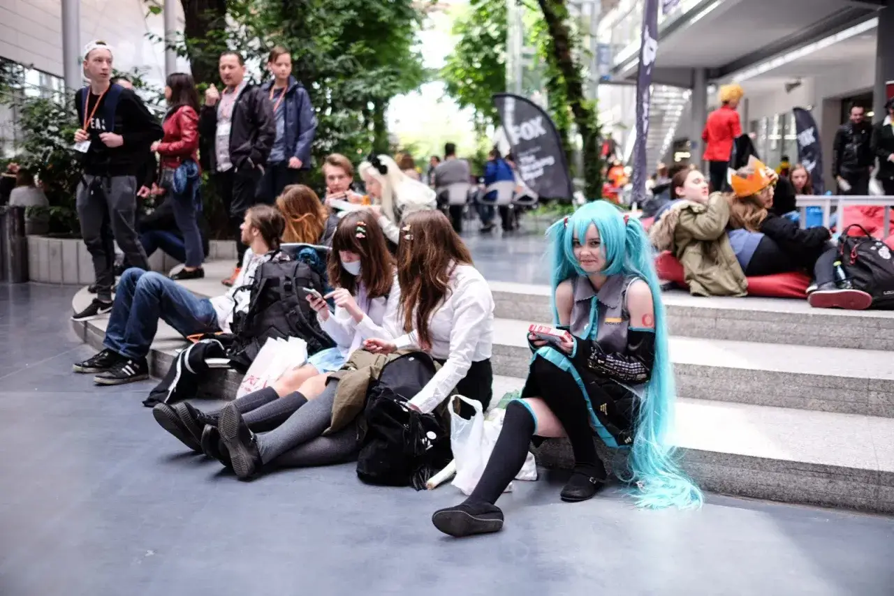 Grupa cosplayerów, w tym dziewczyna w stroju Miku Hatsune, odpoczywa na schodach podczas Pyrkonu w Poznaniu.