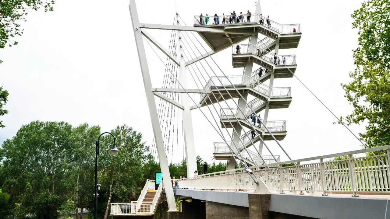 Nowoczesna kładka Owińska z kręconymi schodami i platformami widokowymi, po których spacerują ludzie.