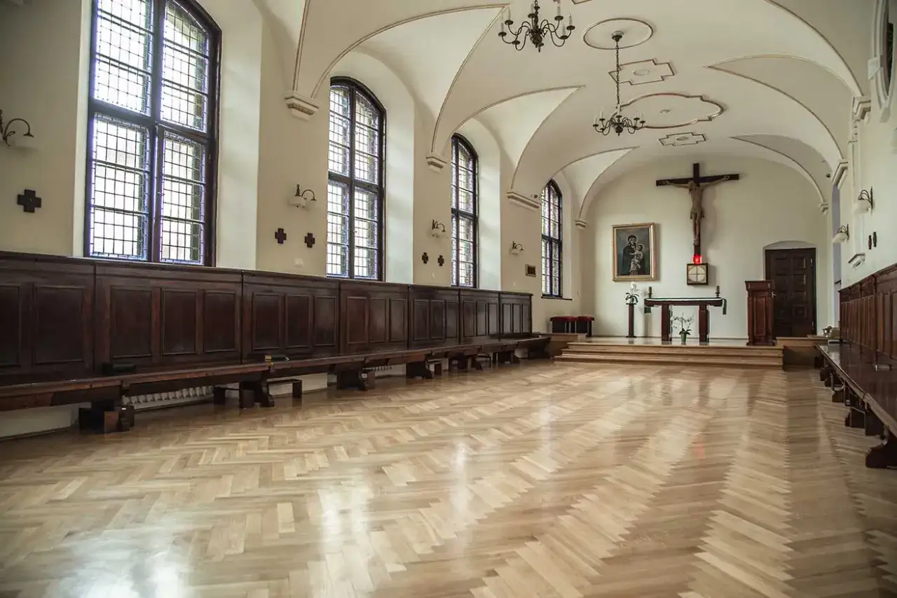 Wnętrze sali modlitewnej Karmelit&oacute;w w Poznaniu. Drewniane ławy, wysokie okna i ołtarz z krzyżem tworzą atmosferę skupienia.