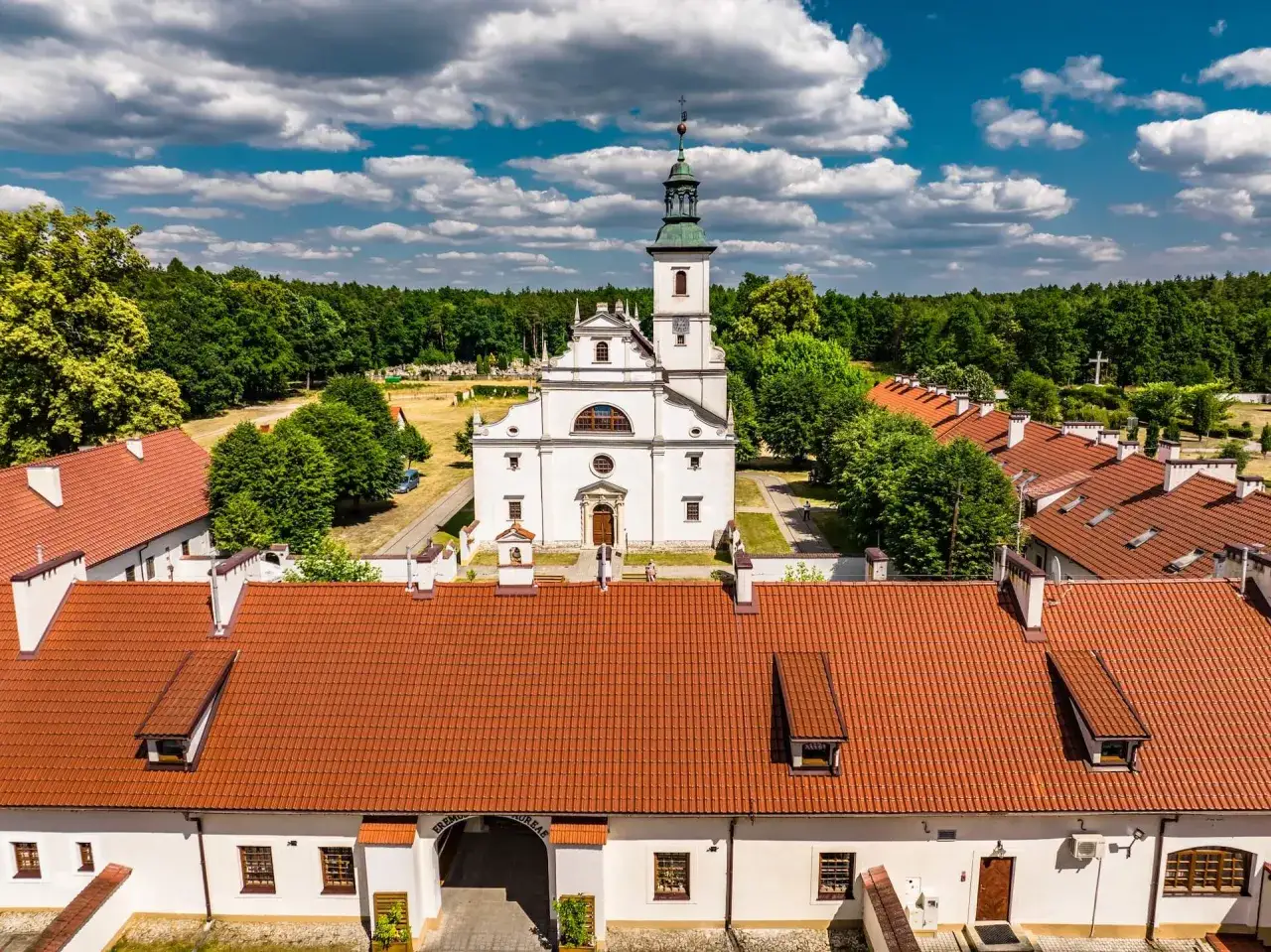 Biały kościół z wieżą i klasztorem, otoczony lasem. Piękne pustelnie w Polsce, gdzie można znaleźć spokój.