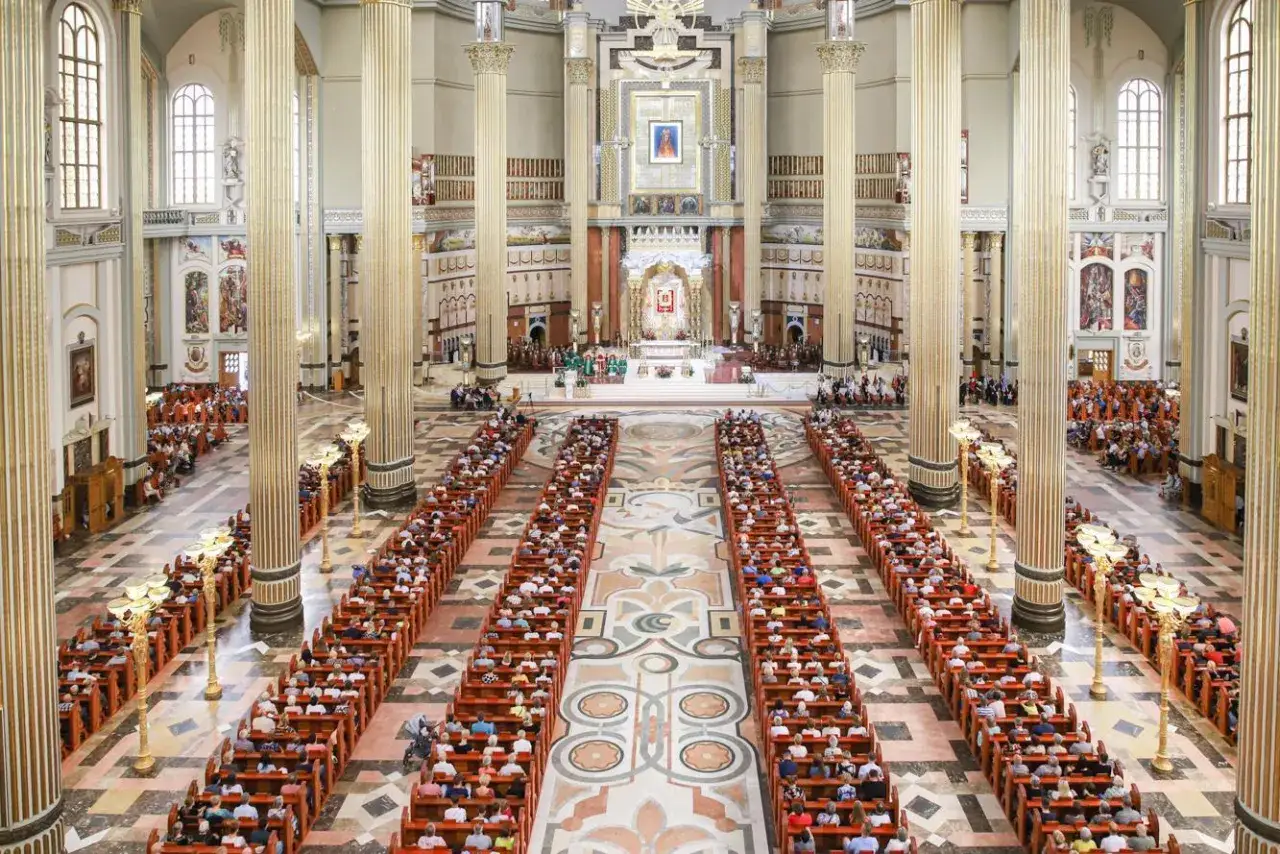 Wnętrze bazyliki w Licheniu wypełnione wiernymi siedzącymi w ławkach. W oddali ołtarz i prezbiterium.