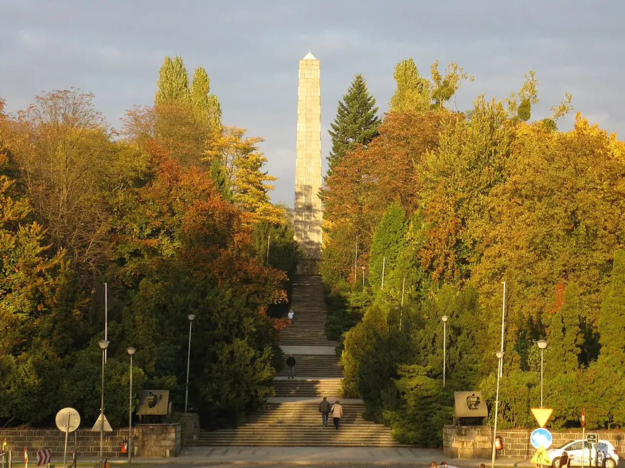 Monumentalne schody prowadzące do obelisku, otoczone jesienną zielenią i złotymi liśćmi. To miejsce przypomina o historii, jakby sama twierdza Poznań opowiadała swoje dzieje.