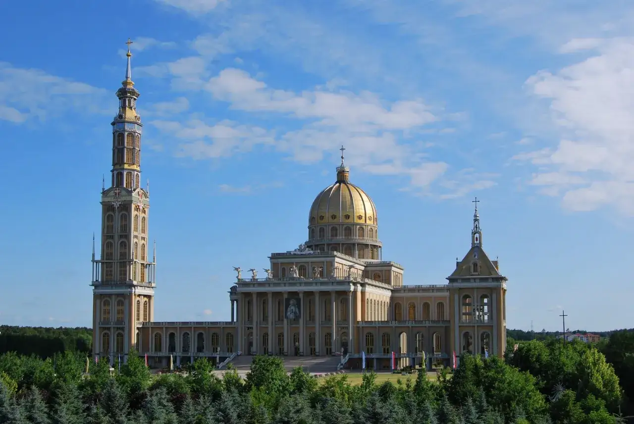 Majestatyczne sanktuarium koło Konina z dominującą złotą kopułą i wysoką wieżą, otoczone zielenią.