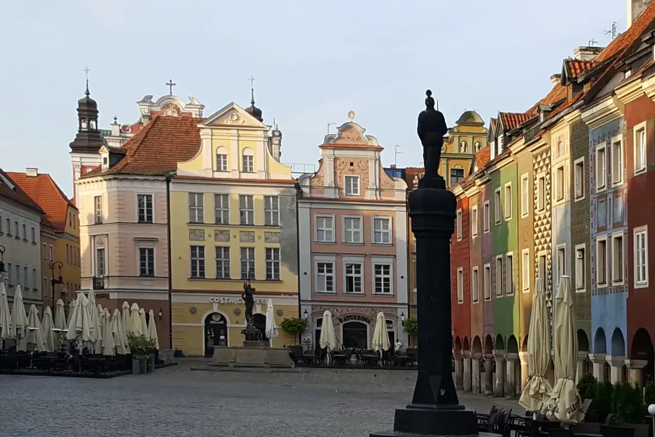 Kolorowe kamienice na poznańskim Starym Mieście, pomnik i zamknięte parasole kawiarniane tworzą malowniczy widok.