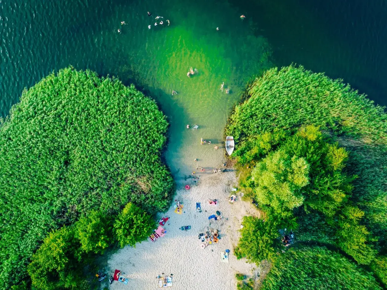Letnie popołudnie nad jednym z najpiękniejszych jezior w Polsce. Ludzie kąpią się, opalają na plaży i relaksują wśród zieleni.