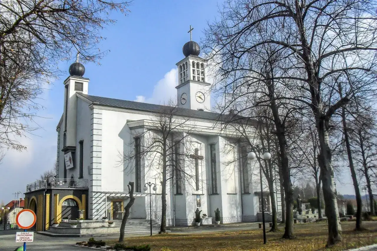 Białe sanktuarium Tursko z wieżą zegarową i krzyżem na fasadzie, otoczone nagimi drzewami.