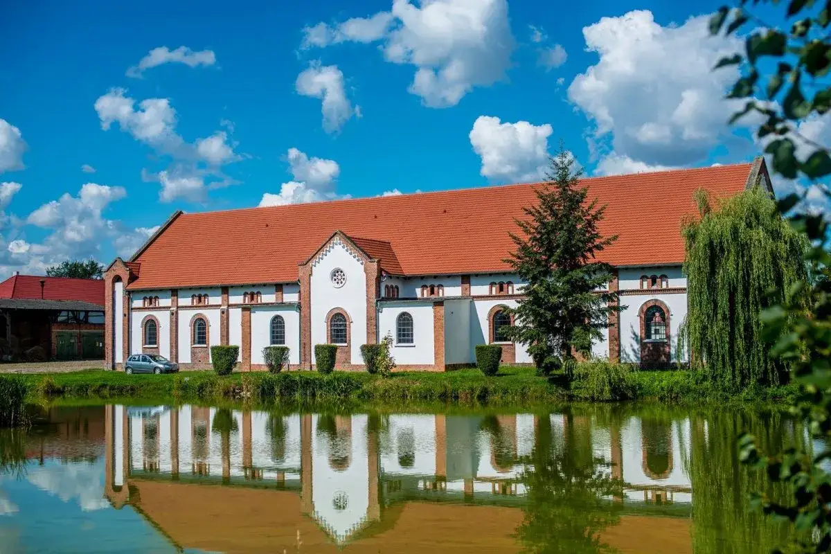Pałac w Racocie z czerwonym dachem i białymi ścianami odbija się w spokojnej tafli wody.