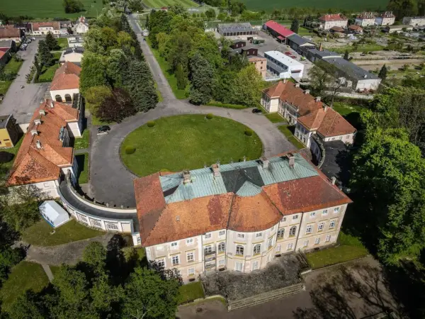 Pałac w Pawłowicach z lotu ptaka, otoczony zielenią i innymi budynkami.