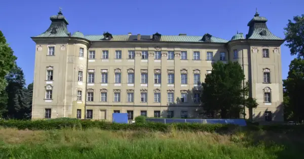 Imponujący pałac, największy zamek w Wielkopolsce, z zielonymi dachami i licznymi oknami, otoczony drzewami i trawą.
