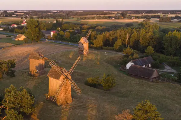 Trzy drewniane wiatraki na tle krajobrazu, przypominające o dawnych pojezierza w polsce.